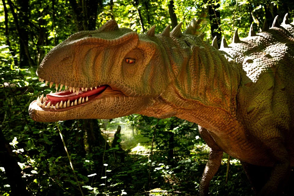 Dinossauro animatrônico de boca aberta entre árvores, em modelo de exposição ao ar livre