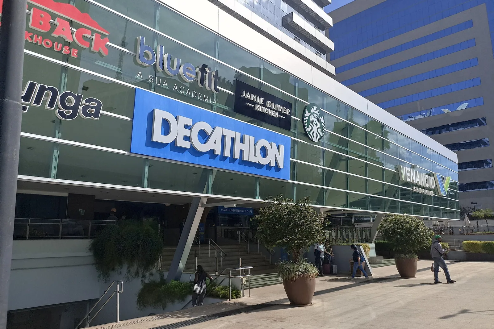 Fachada de vidro do Venâncio Shopping, na Asa Sul, em Brasília, vista da calçada em dia de sol