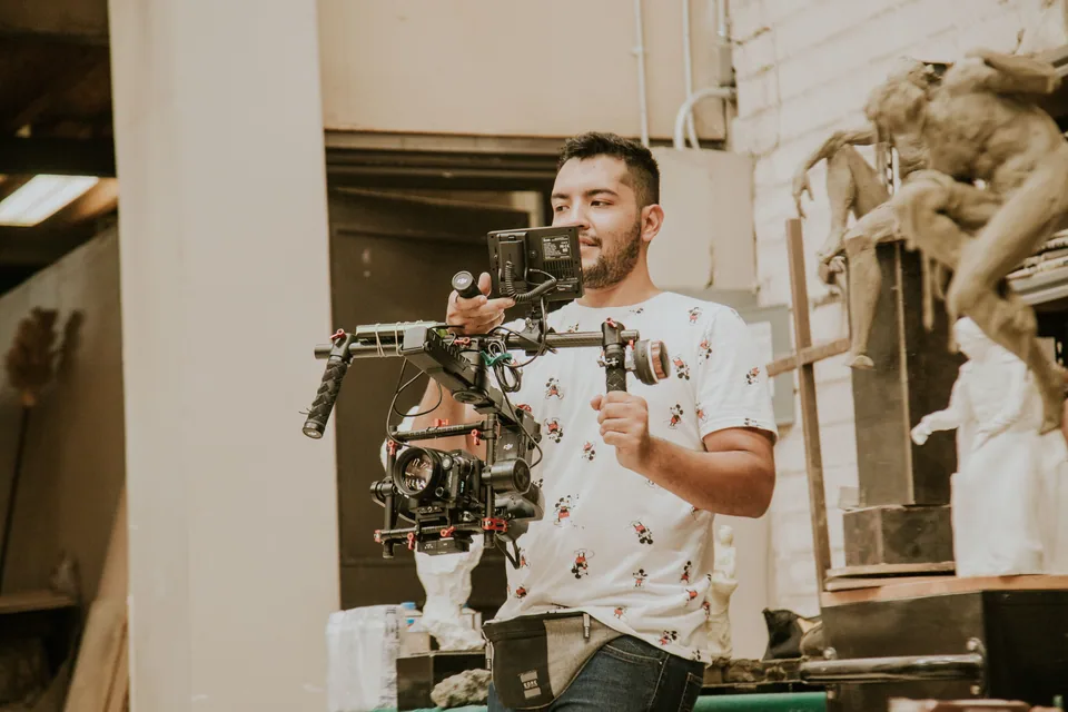 Videomaker segura câmera em estabilizador dentro de um ateliê, em foto ilustrativa