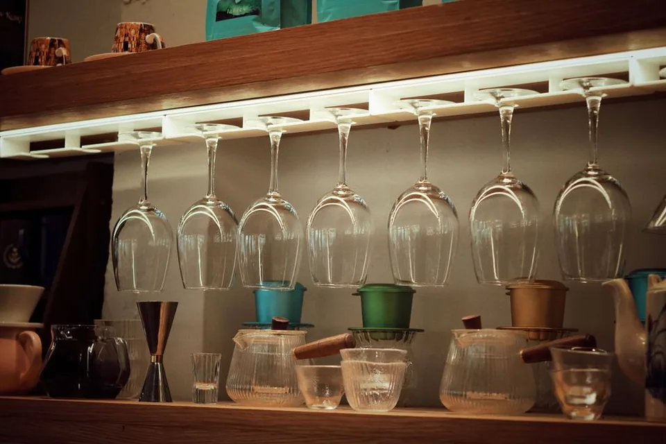 Taças penduradas de cabeça para baixo em um suporte iluminado sobre a bancada de um bar