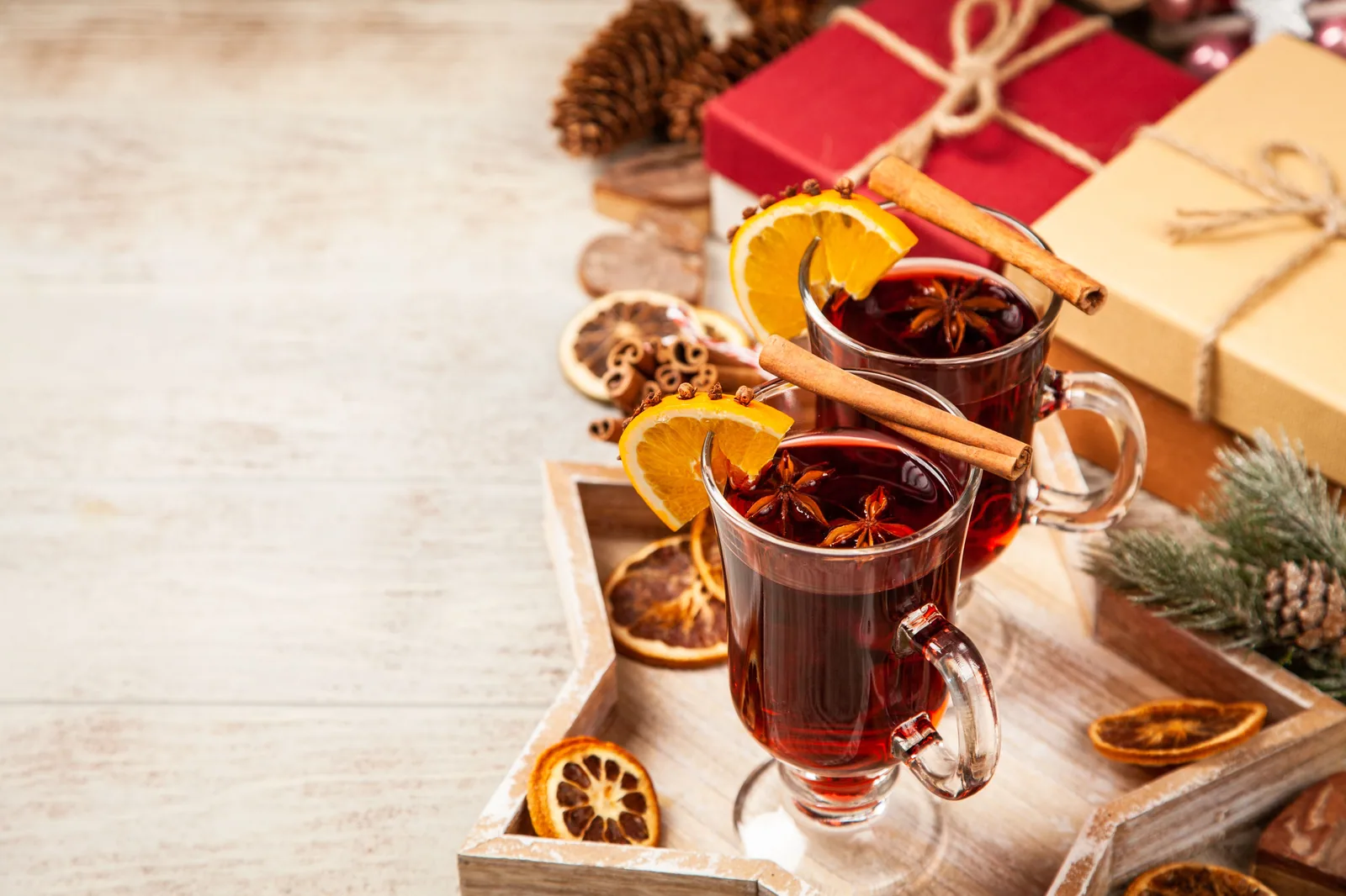 Duas taças de vinho quente com canela, laranja e anis-estrelado ao lado de presentes