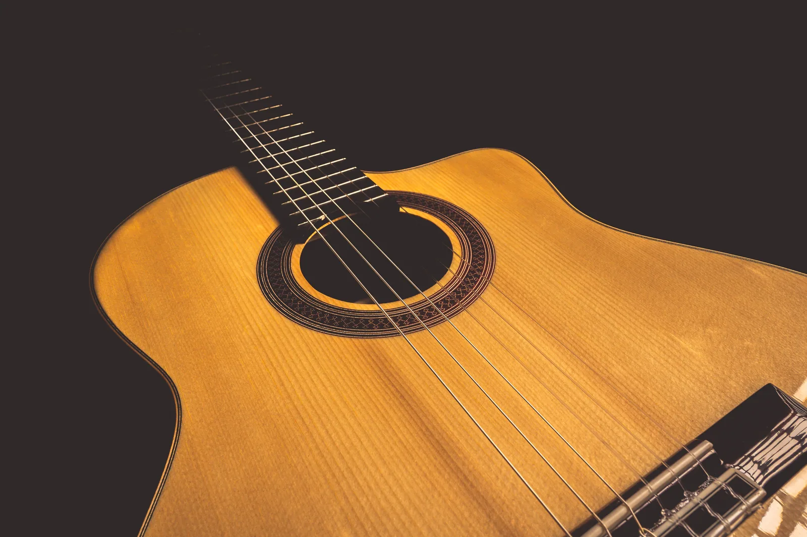 Close de um violão de cordas de náilon, com a boca e o rosáceo em destaque sobre fundo escuro.