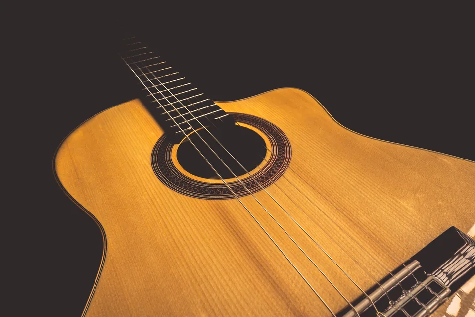 Close de um violão de cordas de náilon, com a boca e o rosáceo em destaque sobre fundo escuro.