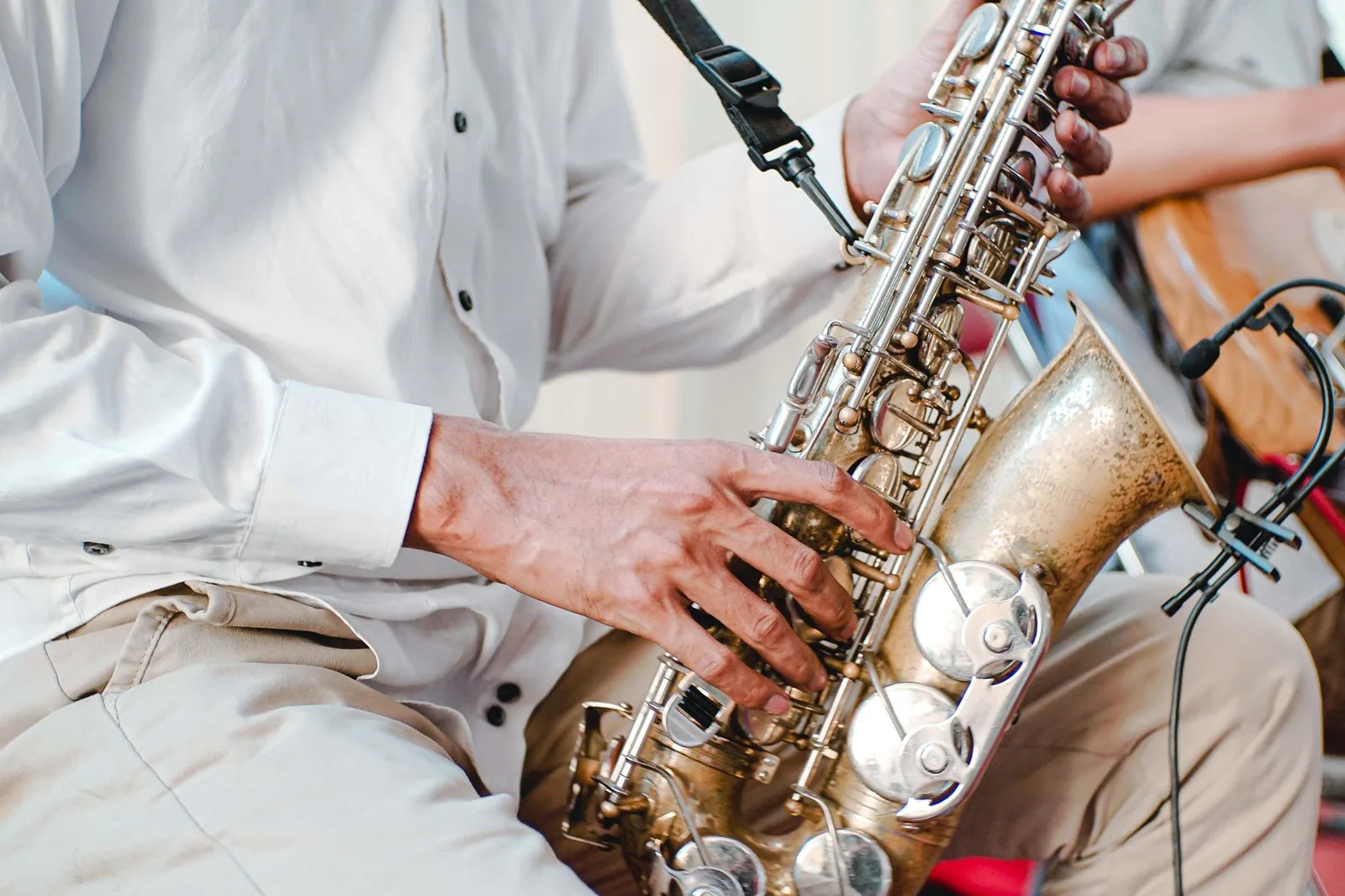 Saxofonista de camisa branca tocando em close, com guitarrista ao fundo