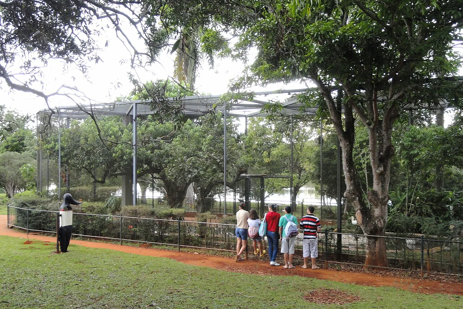 Visitantes diante do viveiro de aves do Zoológico de Brasília, cercado de árvores
